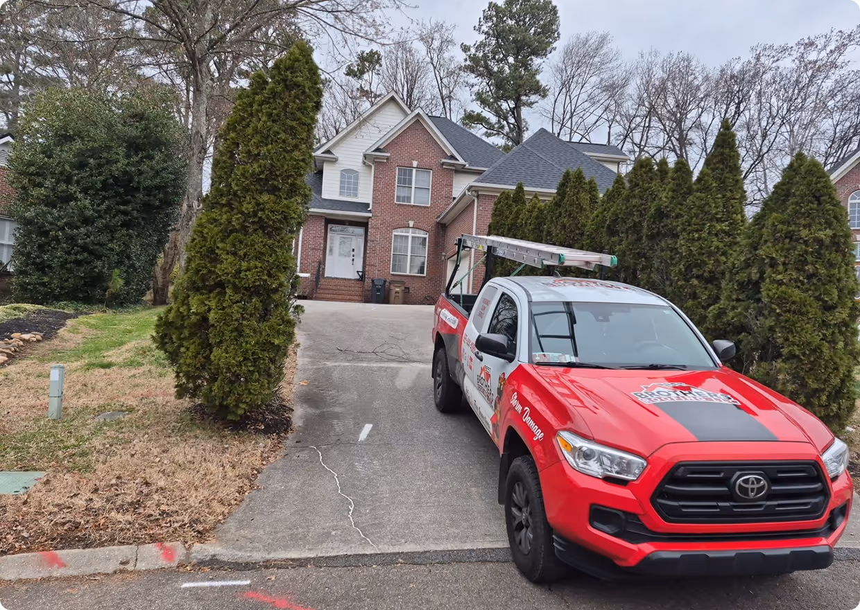 Red and white Toyota pickup truck with a ladder on the rack parked in a driveway in front of a brick two-story house.