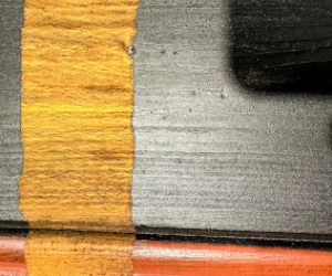 Close-up of a painted surface with yellow, black, and orange sections divided by straight lines.