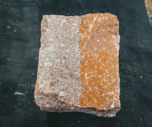 Square stone with one half clean and orange-tinted, the other half dull and gray, placed on a dark surface.