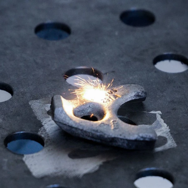 Metal object being precision-cut with sparks flying on a perforated metal surface.