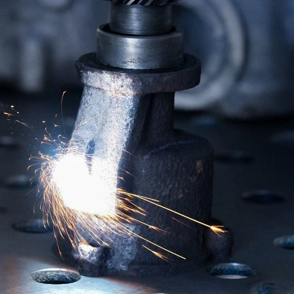 Sparks flying from a metal part being laser cut or welded on a perforated metal surface.