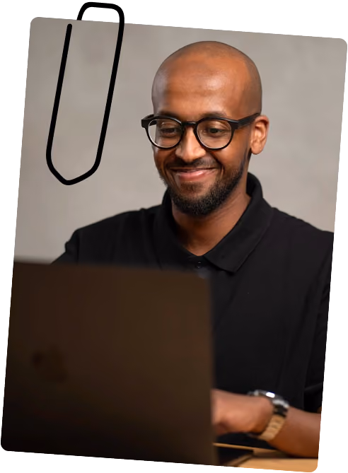 Ein Foto von Ahmed Elmi, während er am Laptop sitzt und lächelt.