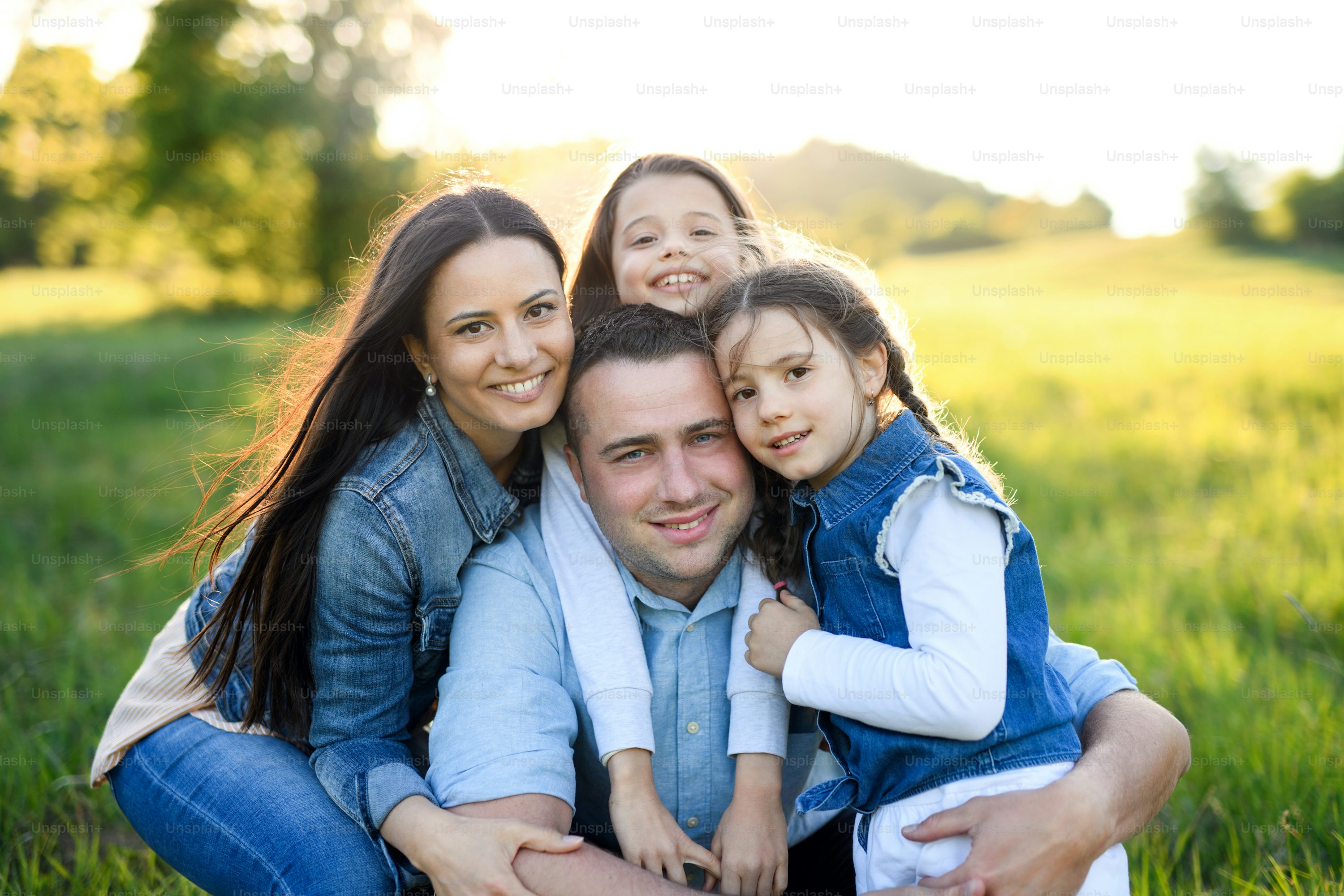 Front view of happy family with two small daughters sitting outdoors in spring nature, looking at camera