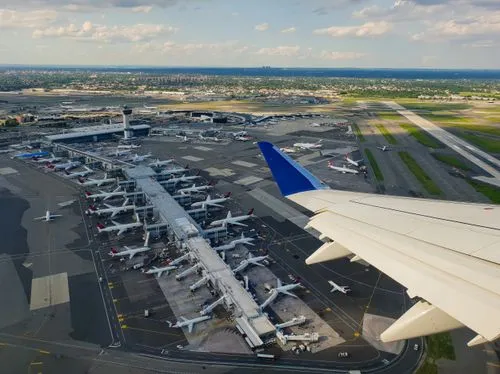 3D model of an airport terminal with glass walls, a control tower, airplane at the gate, and surrounding service vehicles.