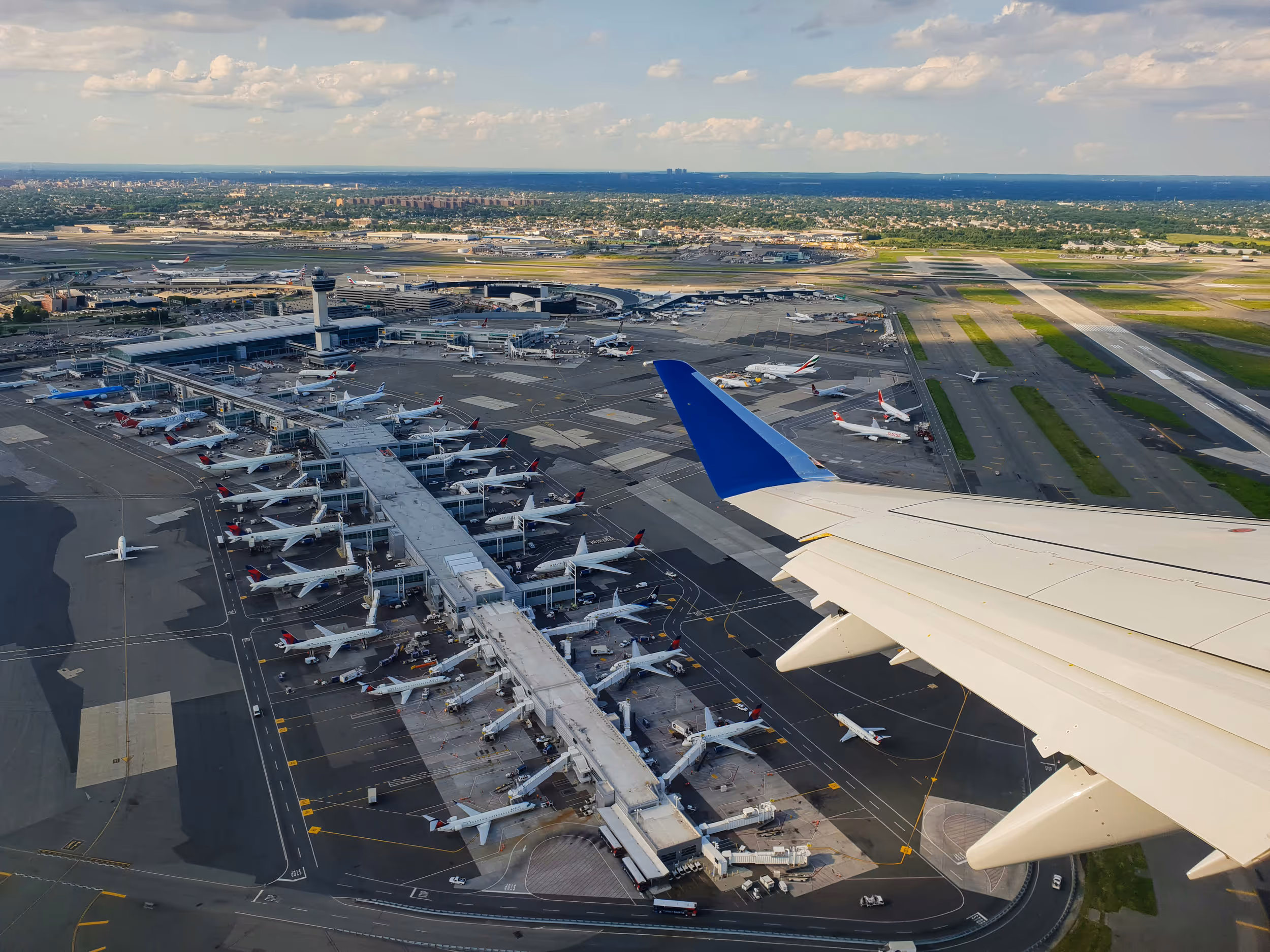 3D model of an airport terminal with glass walls, a control tower, airplane at the gate, and surrounding service vehicles.