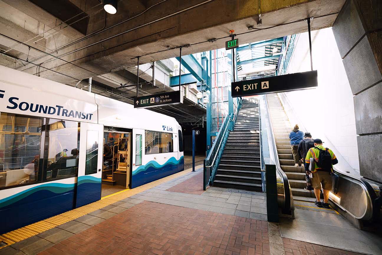 3D model of an airport terminal with glass walls, a control tower, airplane at the gate, and surrounding service vehicles.