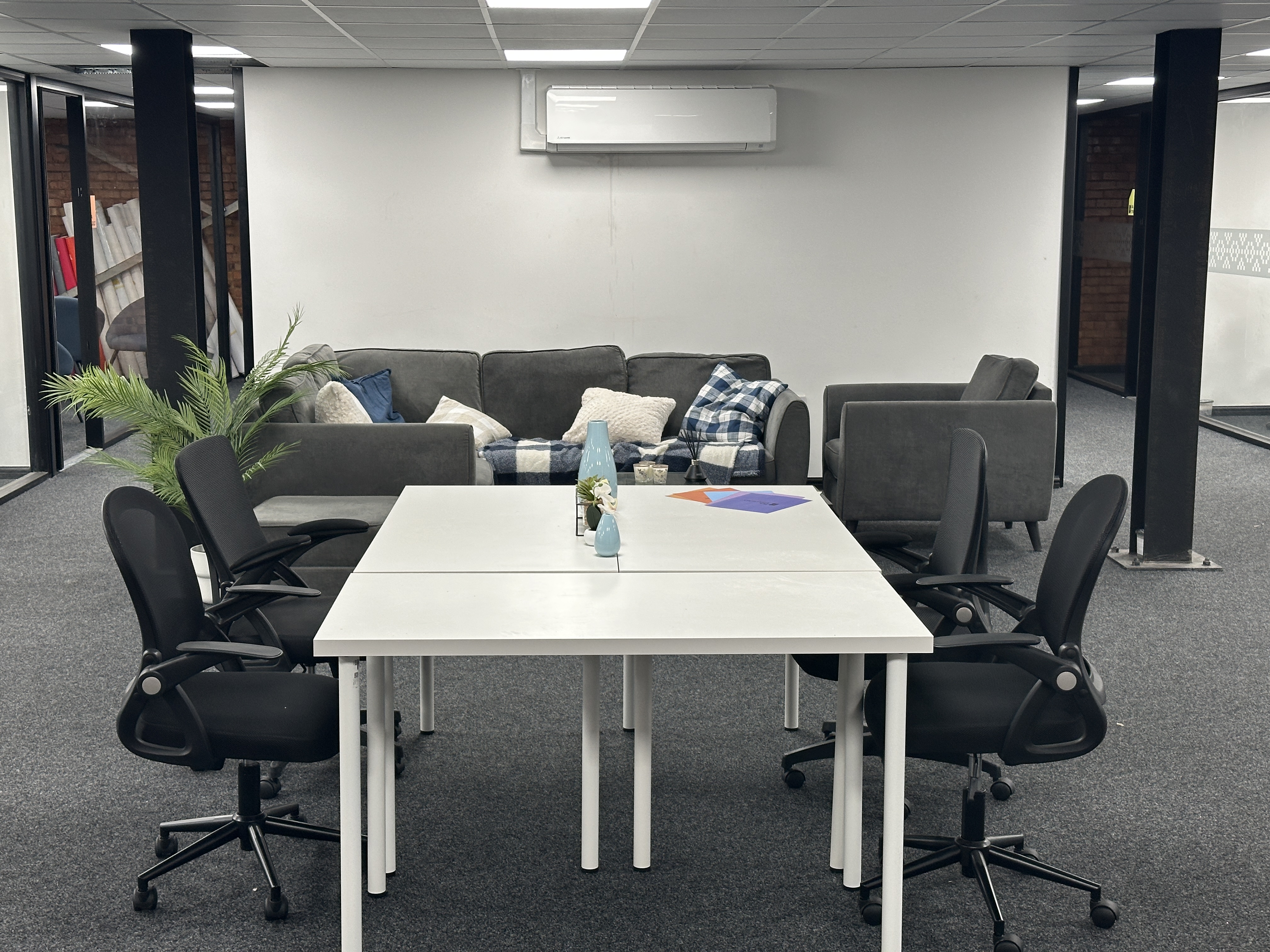 Modern office space with white tables, black swivel chairs, and gray sofas with cushions and a throw blanket.