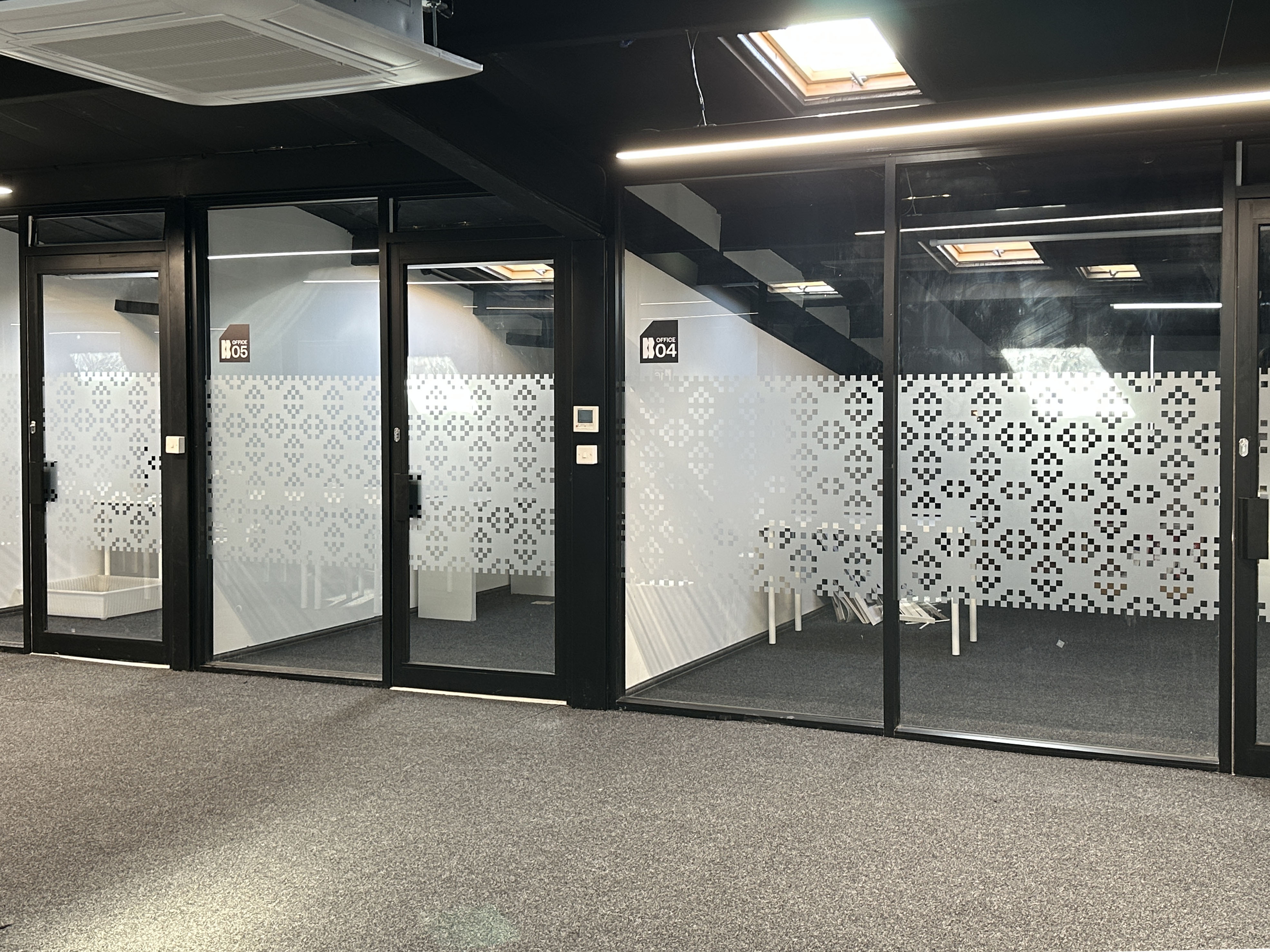 Interior hallway with glass office doors labeled Office 04 and Office 05 with patterned frosted film and gray carpet.