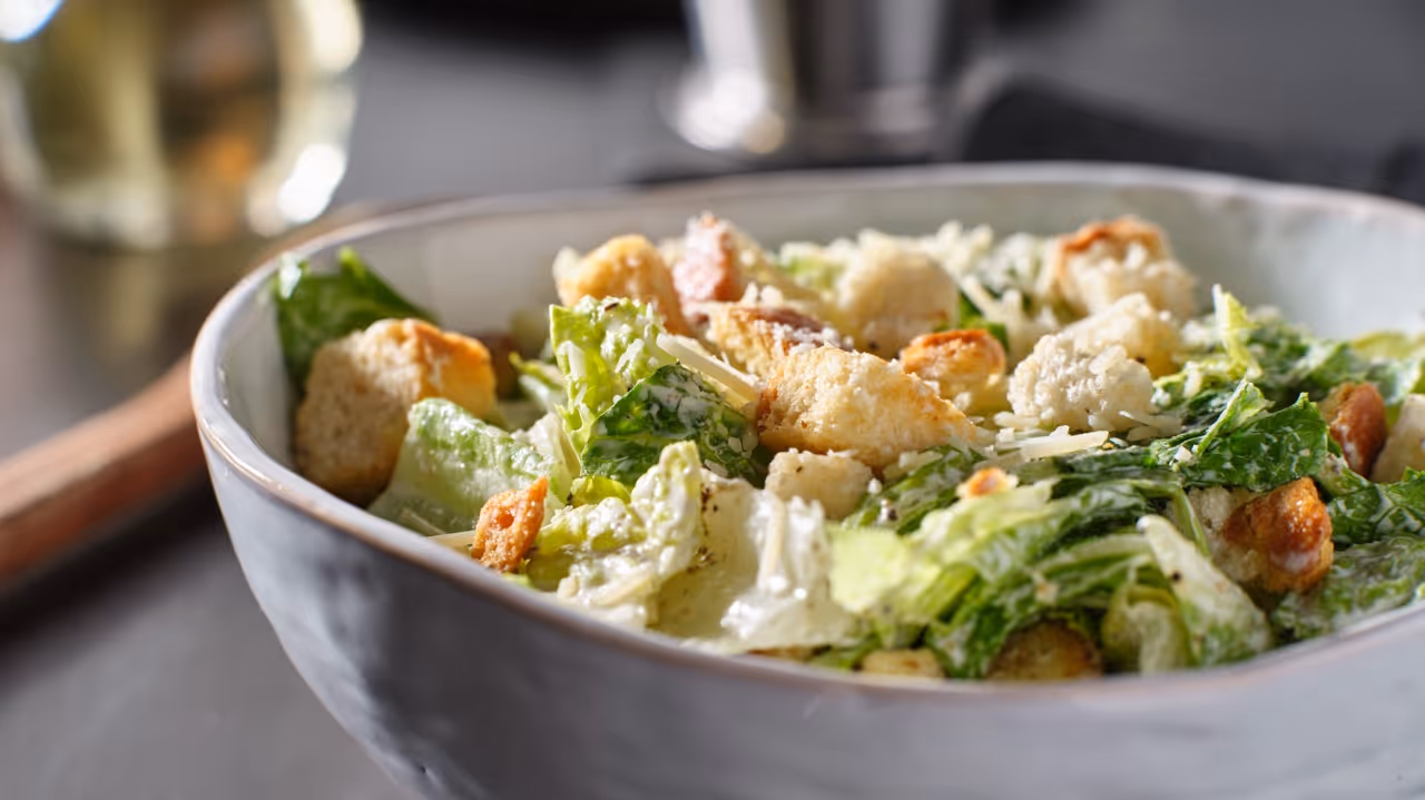 Close-up of Caesar salad with romaine lettuce, croutons, grated cheese, and creamy dressing in a bowl.
