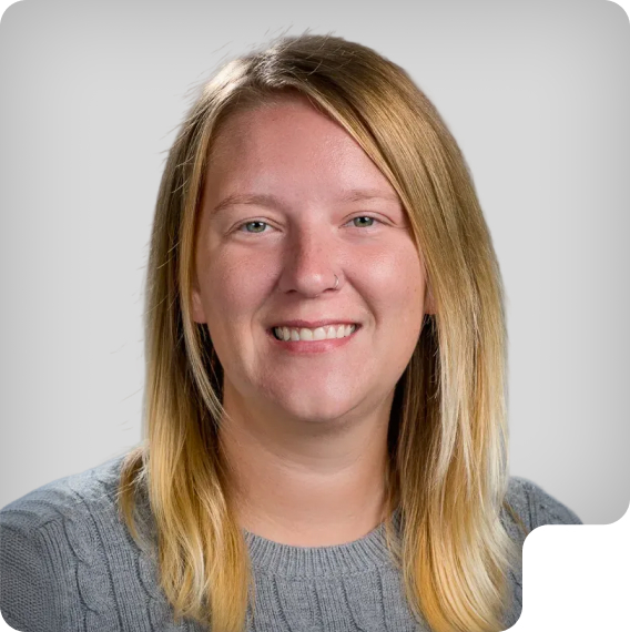 Kristie with straight blonde hair wearing a grey cable-knit sweater against a light grey background.