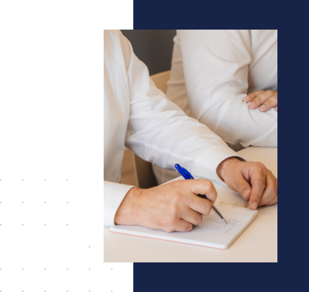 Deux personnes en chemises blanches, l'une prenant des notes dans un carnet à spirale avec un stylo bleu.