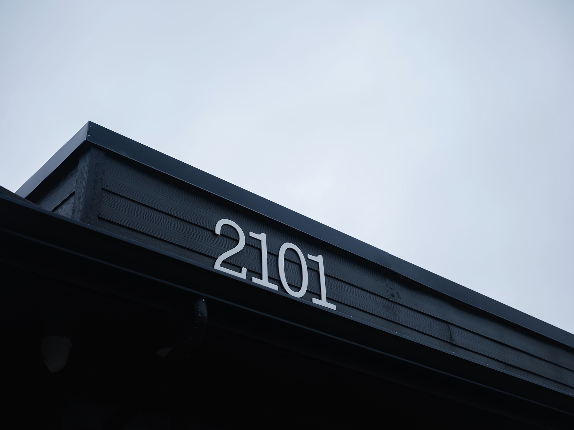 White house number 2101 displayed on black wood exterior under an overcast sky.