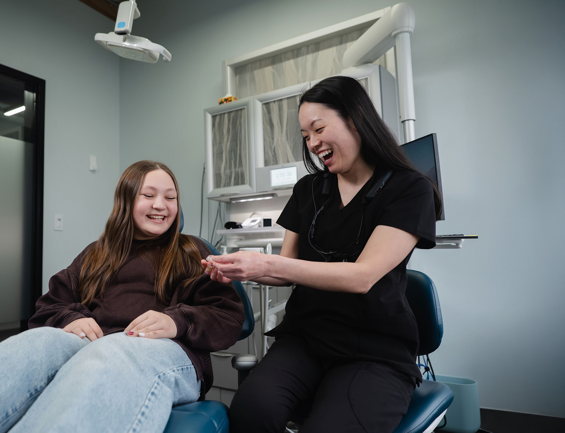 Smiling female dentist showing a dental tool to a relaxed girl in a dental clinic chair.