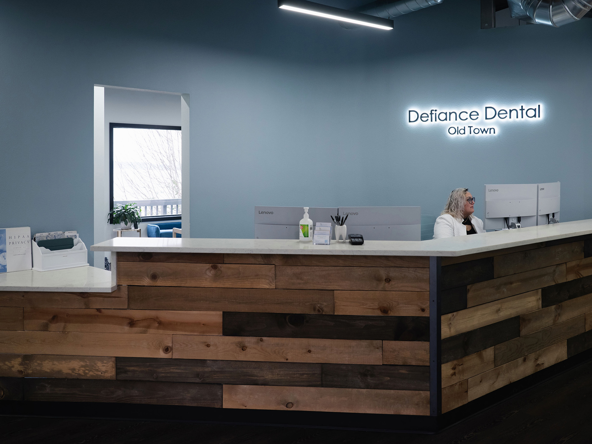 Reception desk with wood paneling and a woman seated under a Defiance Dental Old Town sign.