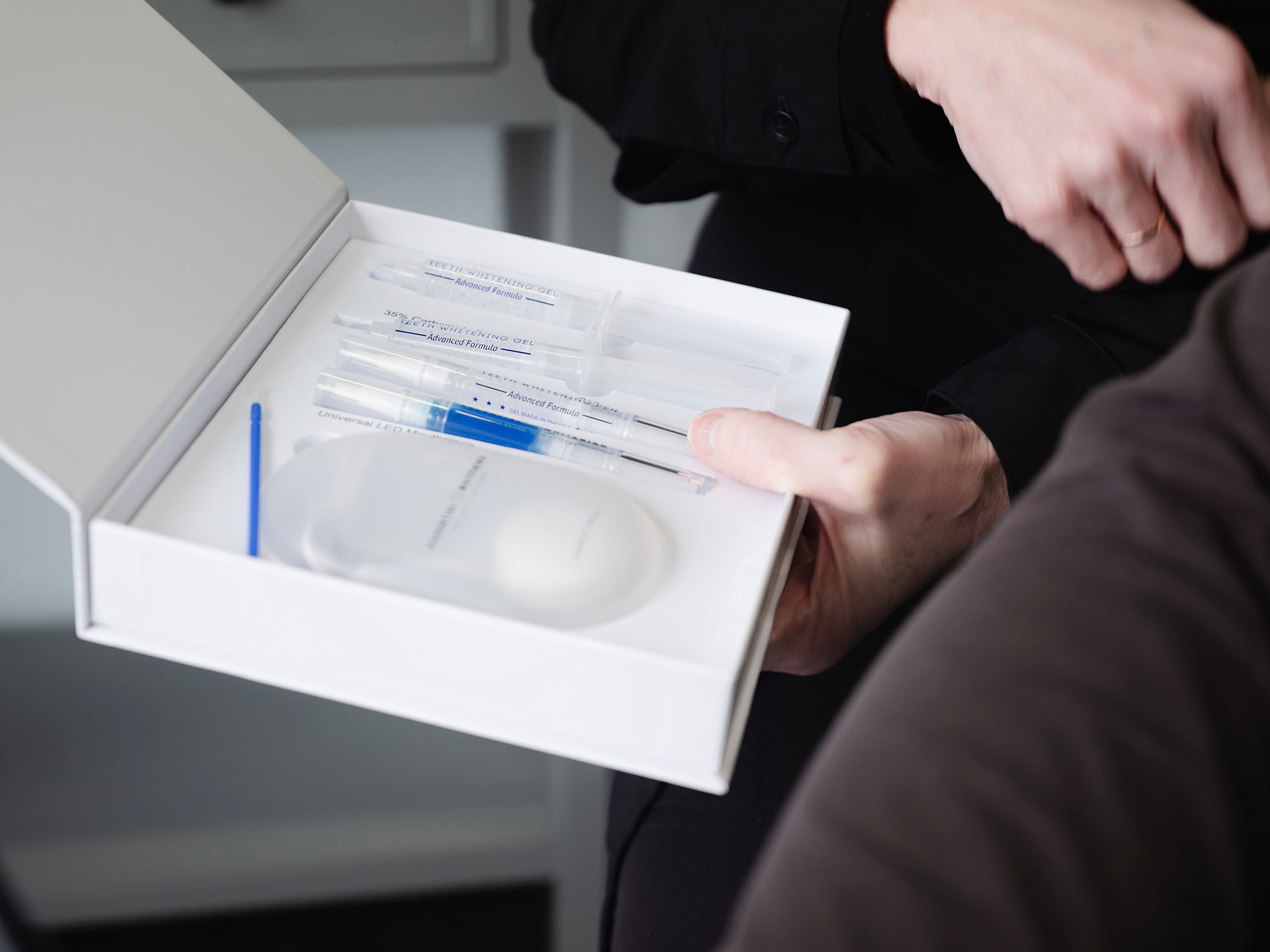 Person holding an open teeth whitening kit with syringes, gel, and LED mouthpiece inside.