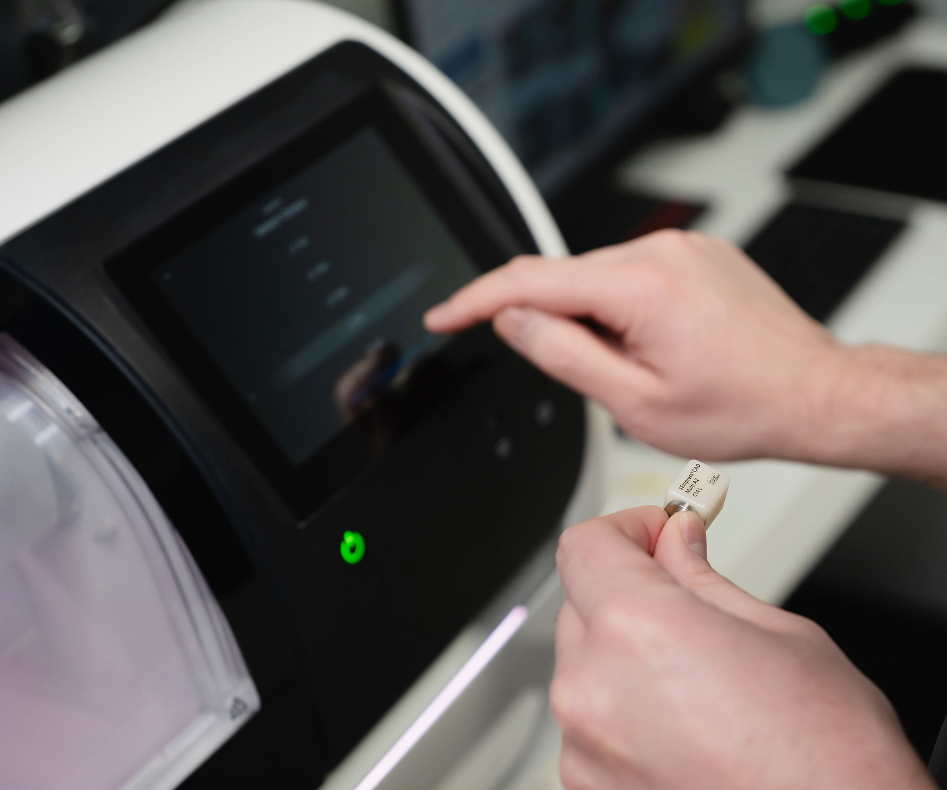 Hands operating a device touchscreen while holding a small labeled dental crown model.