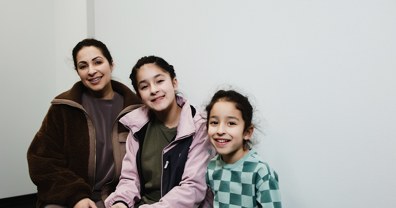 Smiling woman with two girls posing indoors against a plain white wall.