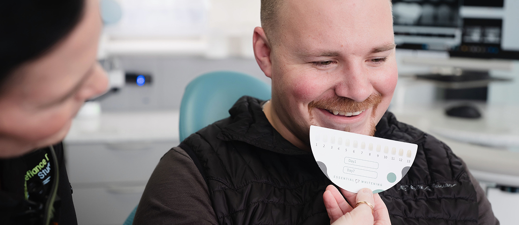 Man smiling while holding a teeth shade guide in a dental clinic.