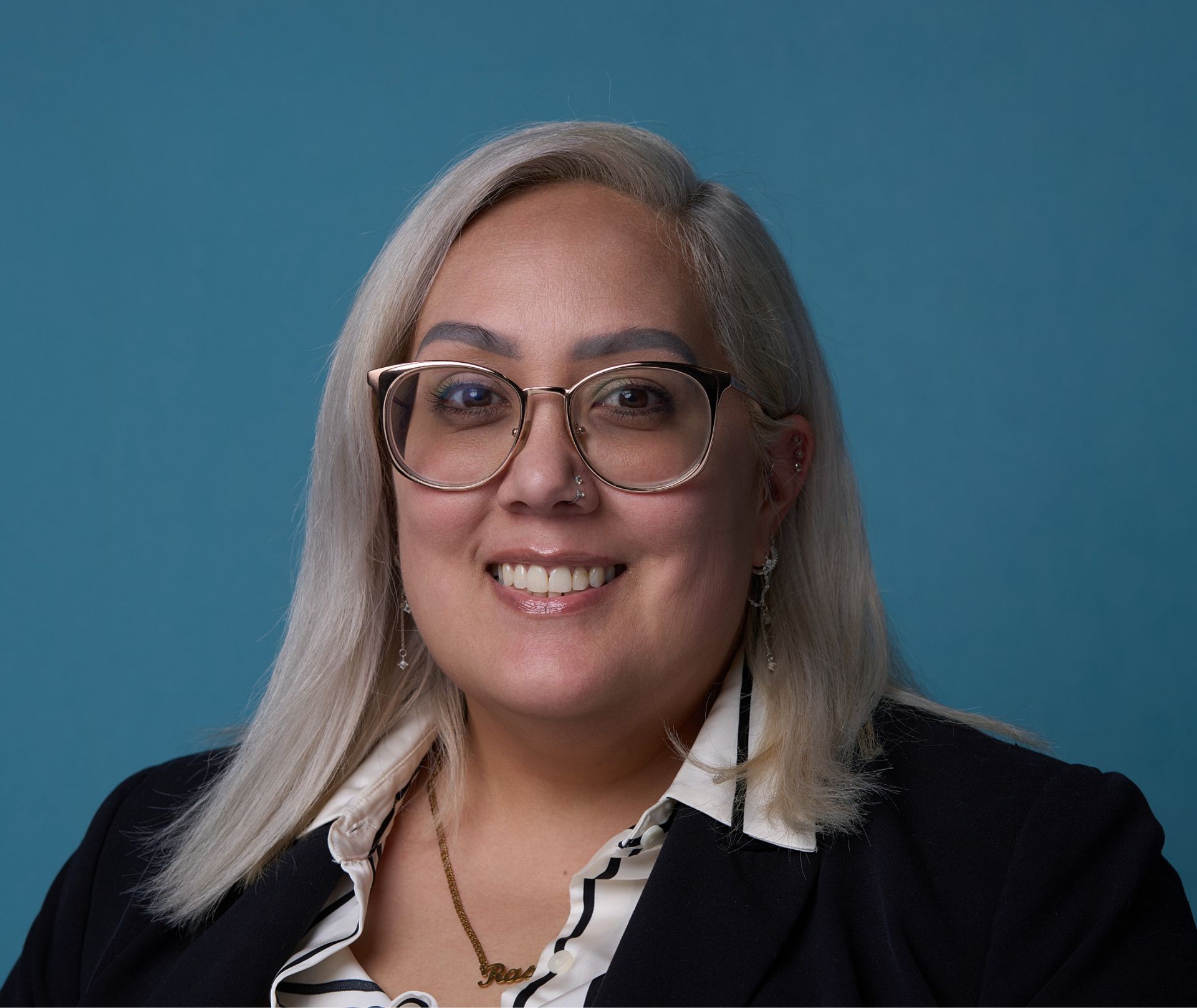 Smiling woman with blonde hair, glasses, and a black blazer poses against a blue background.