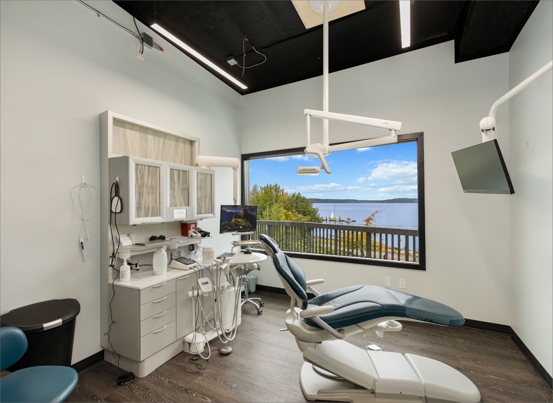 Modern dental office with patient chair and large window overlooking waterfront and trees.