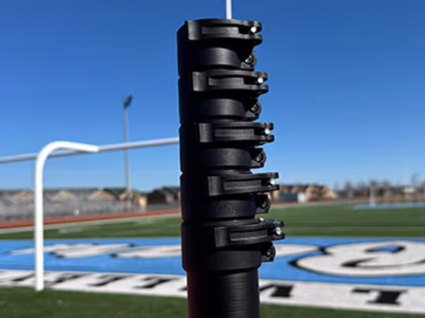 Close-up of a black adjustable pole with multiple clamps on a sports field with a clear blue sky.