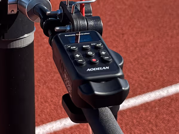 Close-up of an AODELAN remote controller mounted on a tripod with a red sports track background.