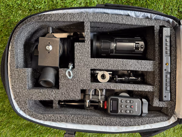 Open case with custom foam insert holding a video camera, remote control, and mounting accessories on green grass.