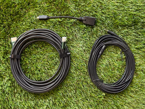 Two coiled black cables and one black adapter cable laid out on green grass.