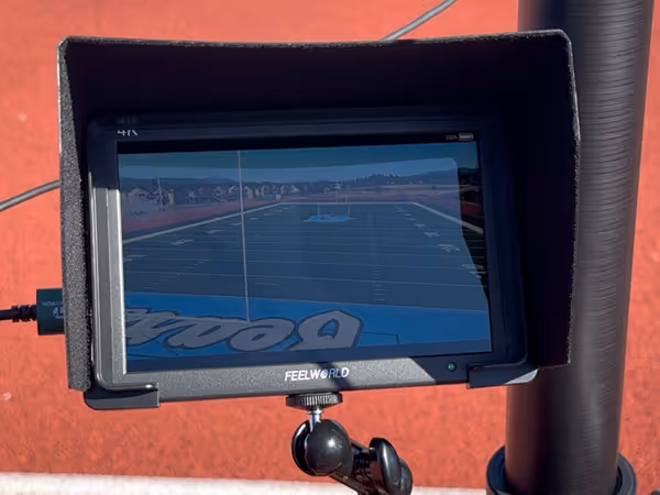 FEELWORLD monitor displaying a football field with end zone text and surrounding track, mounted outdoors with a sunshade.