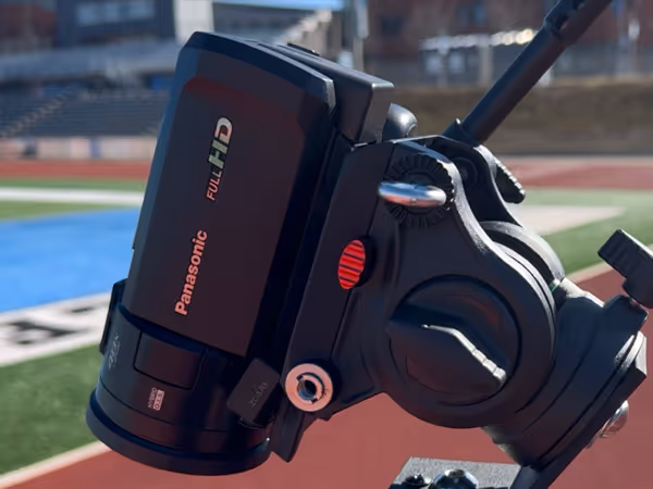 Close-up of a Panasonic Full HD video camera mounted on a tripod at an outdoor sports field.