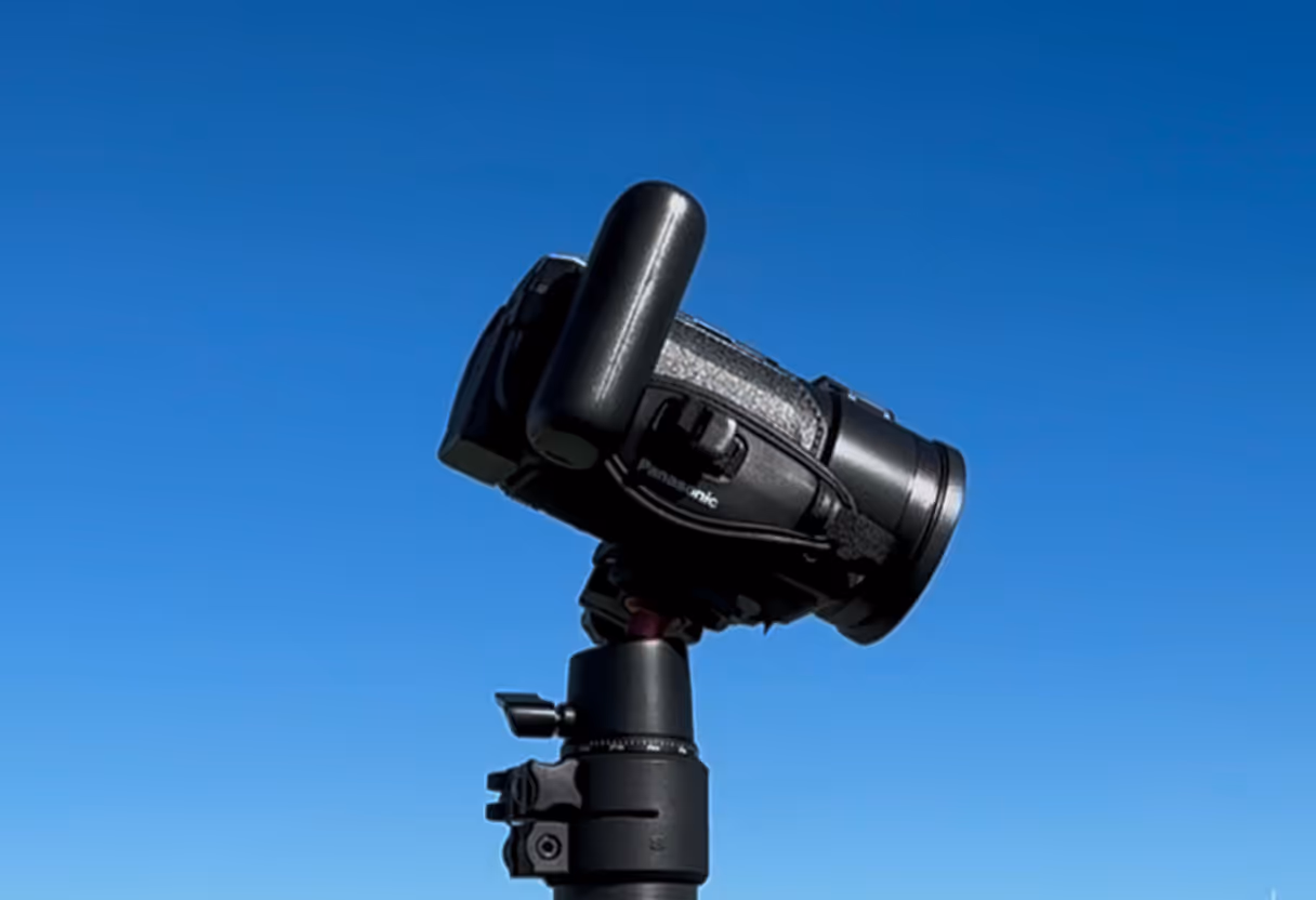 Black Panasonic video camera mounted on a tripod against a clear blue sky.  Showing the tilt of a camera on an end zone camera.