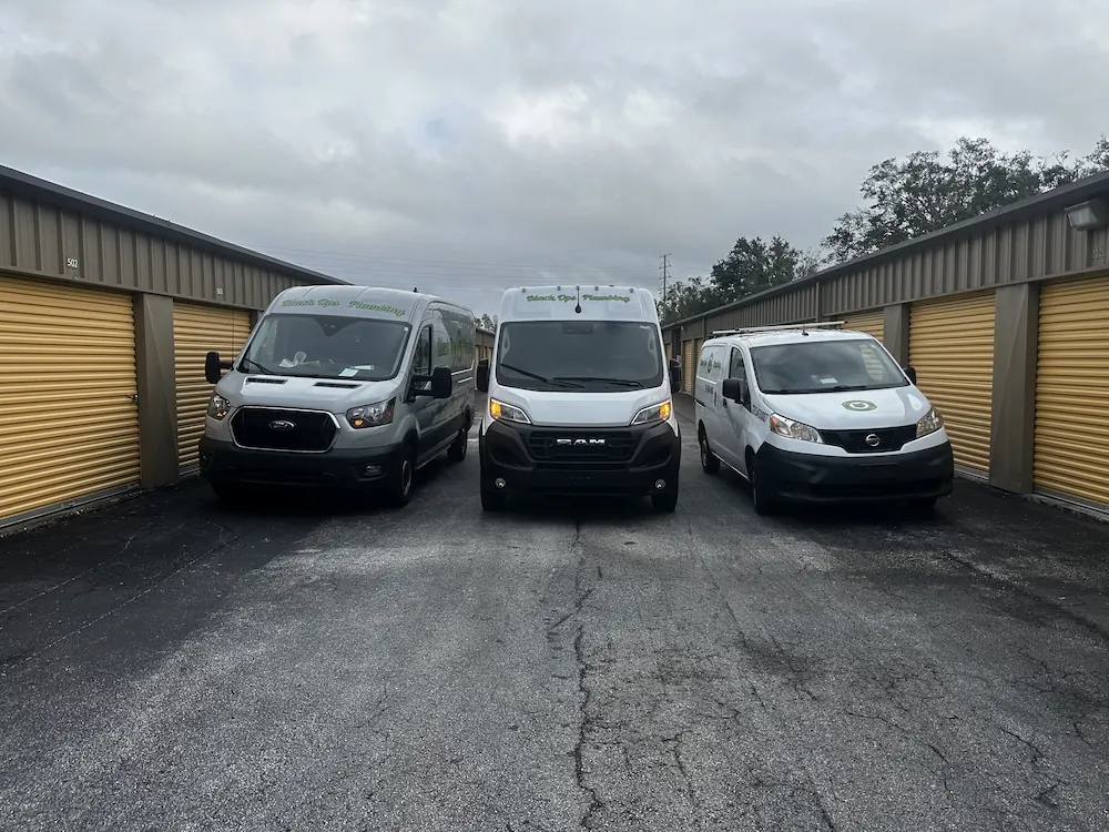 Three vans parked side by side between two rows of yellow storage unit doors under a cloudy sky.
