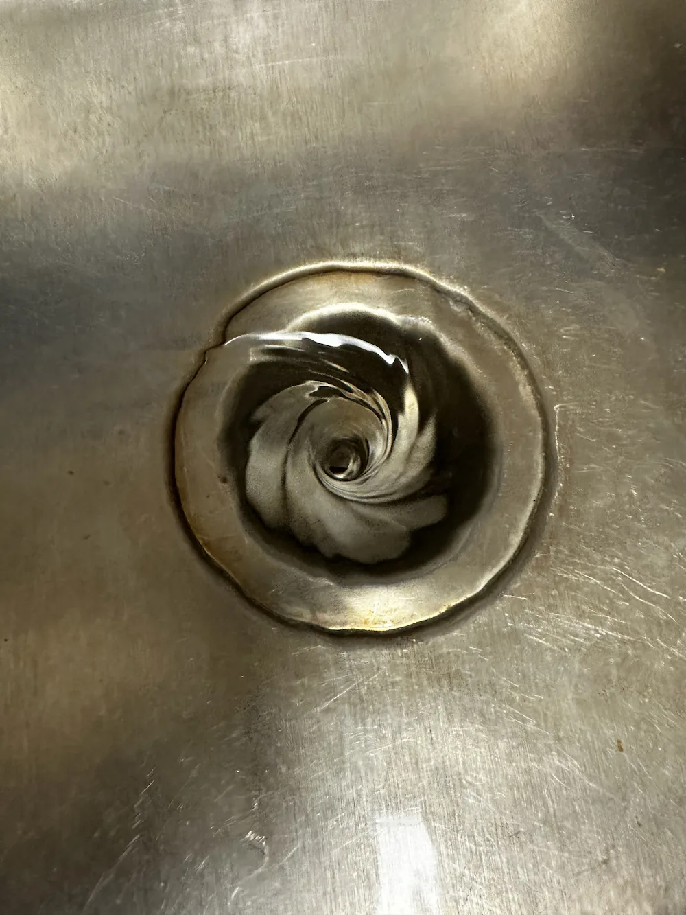 Close-up of water swirling down a metal drain in a sink.