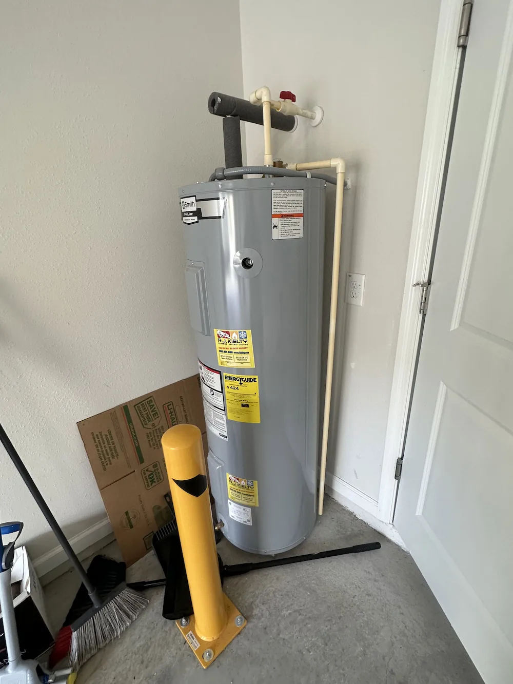 Gray A.O. Smith ProLine water heater installed in a corner with nearby cleaning tools and a yellow bollard.