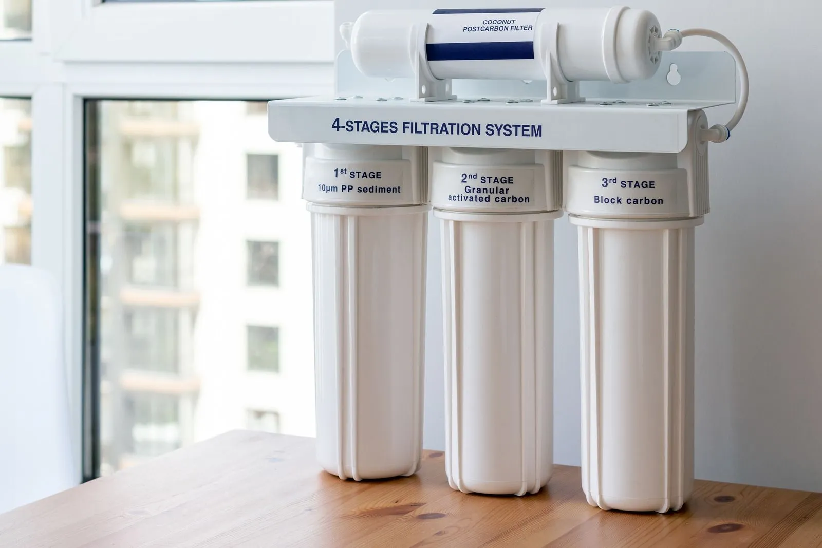 Four-stage water filtration system with labeled filters including sediment, granular activated carbon, block carbon, and coconut post-carbon filter.