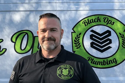 Man with short hair and beard wearing a Black Ops Plumbing polo shirt standing in front of a van with the Black Ops Plumbing logo.