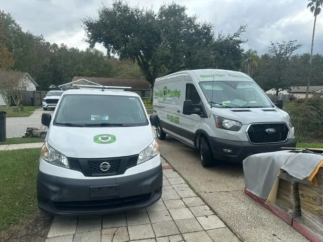 White Nissan van and silver Ford van parked on a residential driveway with green lawn and trees in the background.