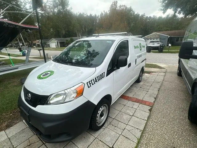 White Nissan work van parked on a driveway with green and black company logo and text on hood and side.