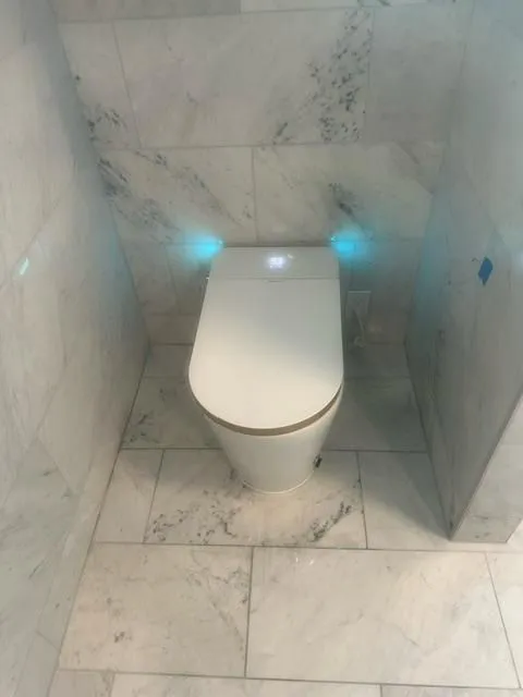Modern white toilet with closed lid in a small bathroom with light gray marble tiled walls and floor.