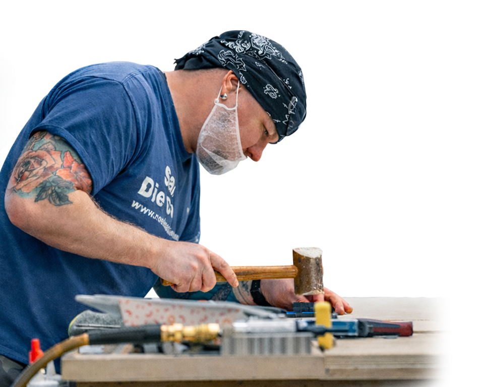 An image of a man using a mallet at a work bench.
