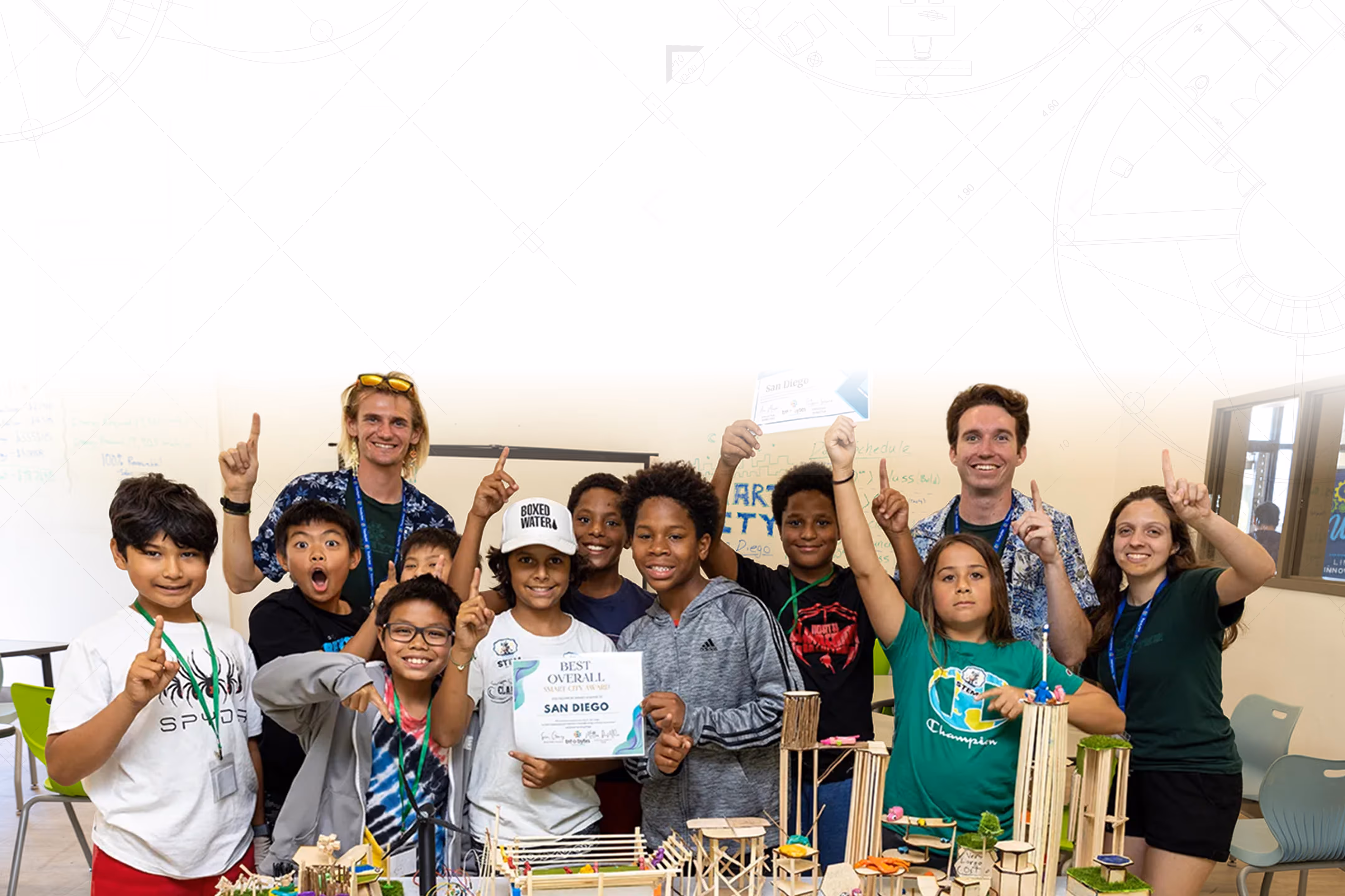A group of smiling children and two adults proudly hold certificates and pose behind a table with miniature architectural models.