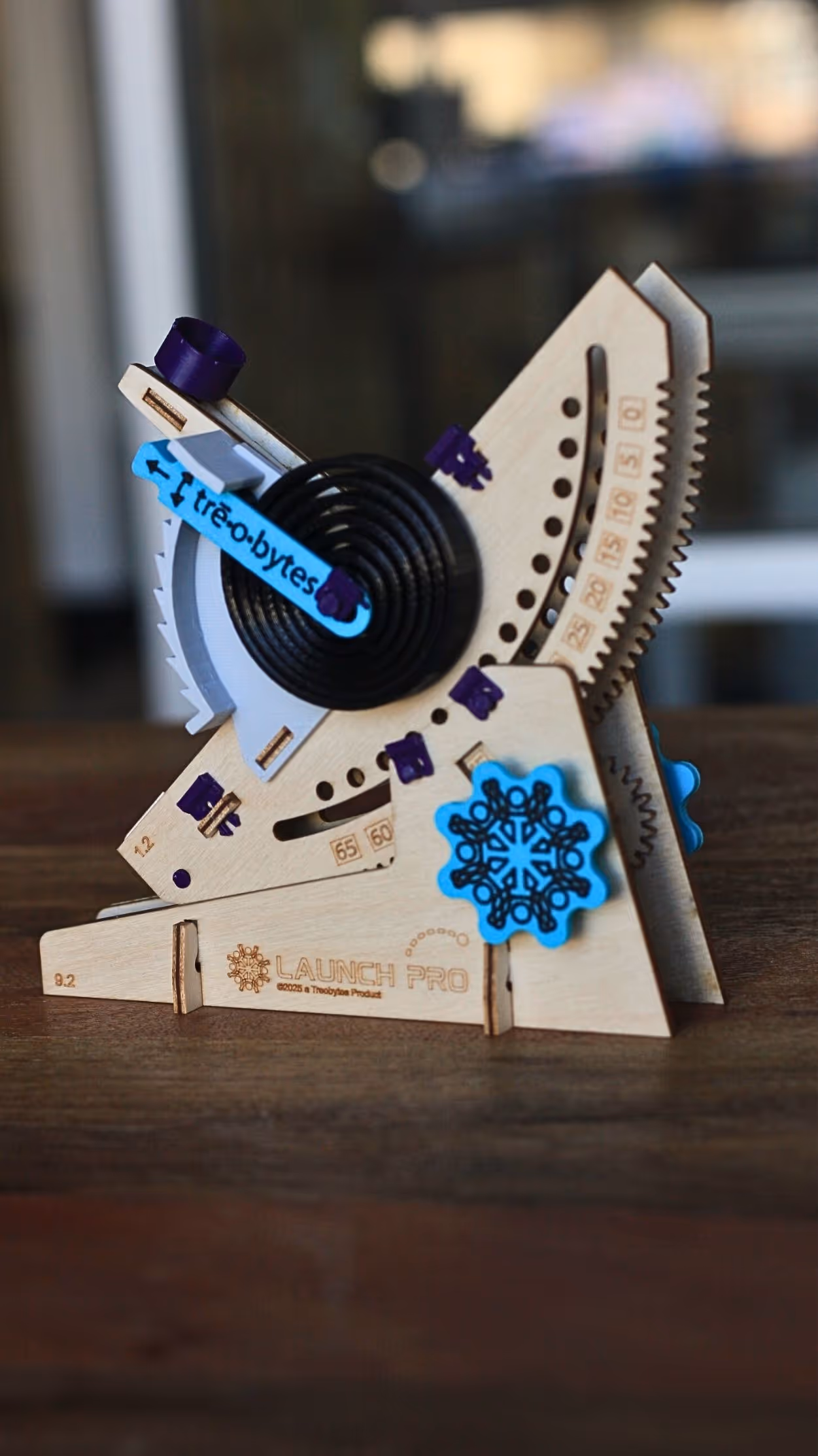 Wooden mechanical device labeled 'Launch Pro' with blue and purple plastic components on a wooden surface.