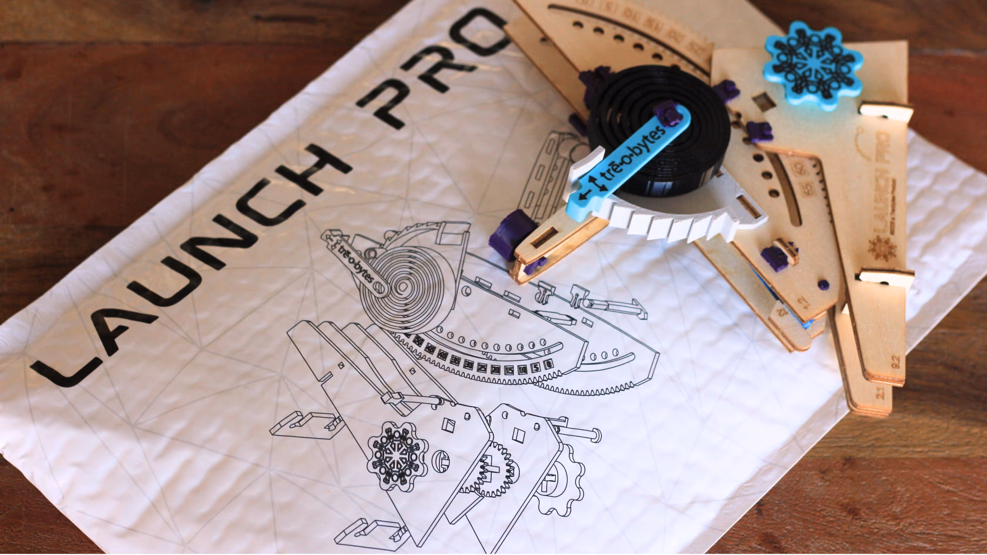 Wooden pieces and a black tape measure laid on a white mailer with a technical drawing and text 'LAUNCH PRO'.