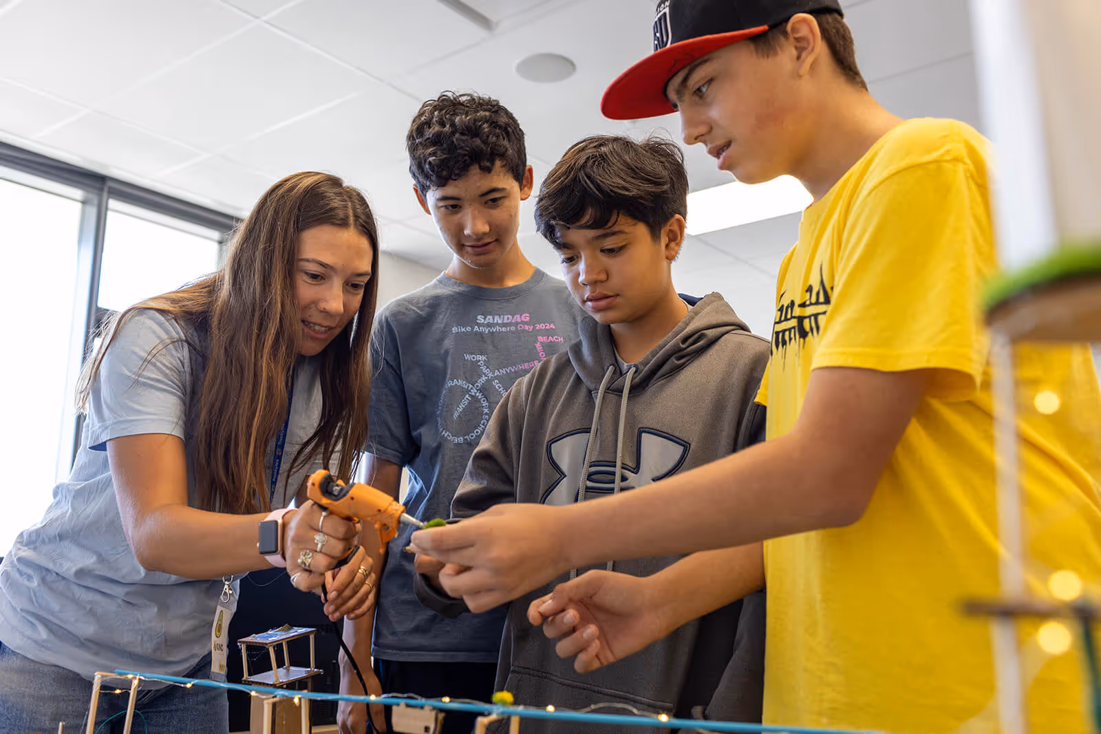 A smiling woman in a beige blazer shakes hands with a woman in a blue shirt holding a green folder in a classroom setting.