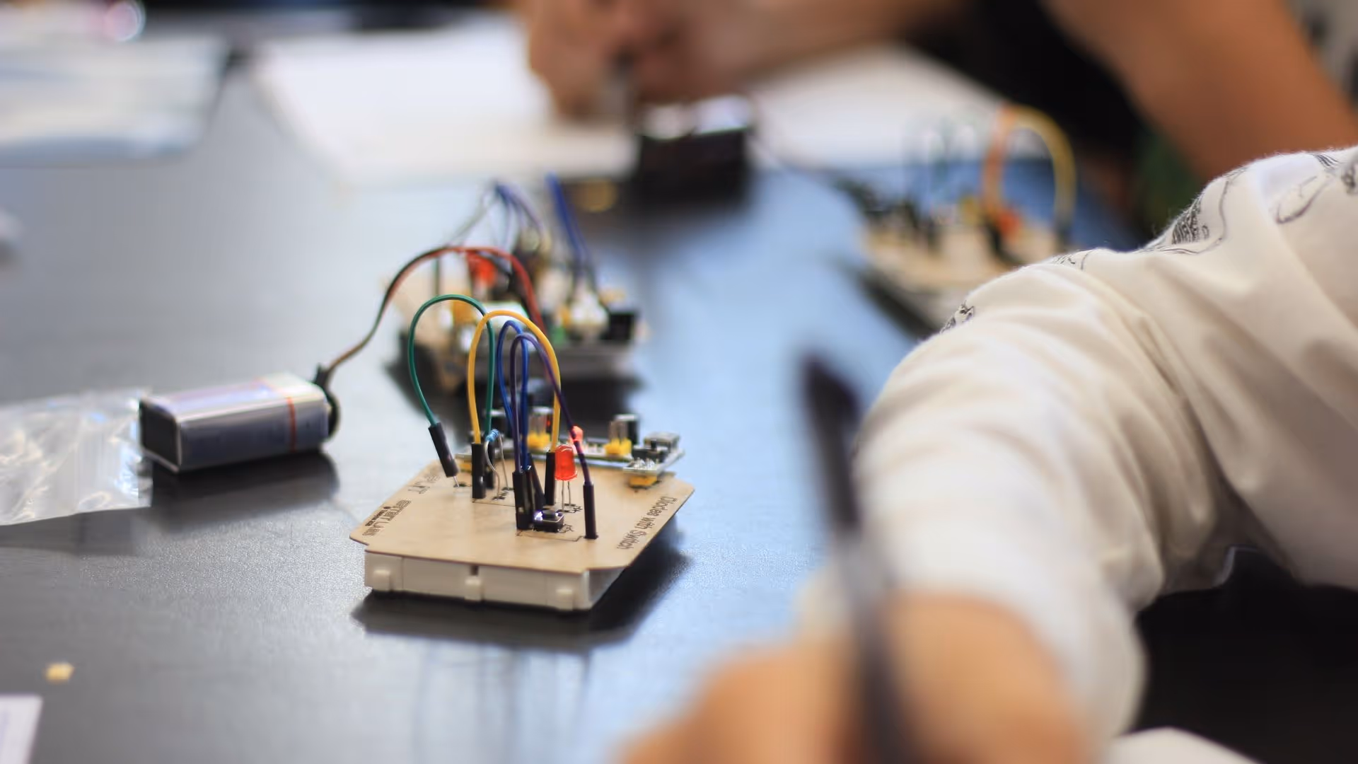 Hands-on electronics project with breadboard, jumper wires, and 9V battery on a table.