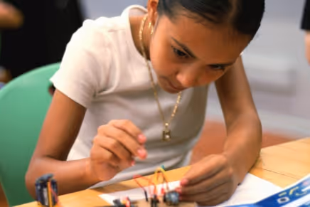 Boy working on a cardboard electronics project labeled 'Let it go' on a classroom table.