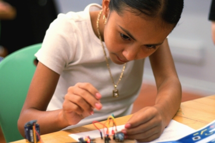 Boy working on a cardboard electronics project labeled 'Let it go' on a classroom table.