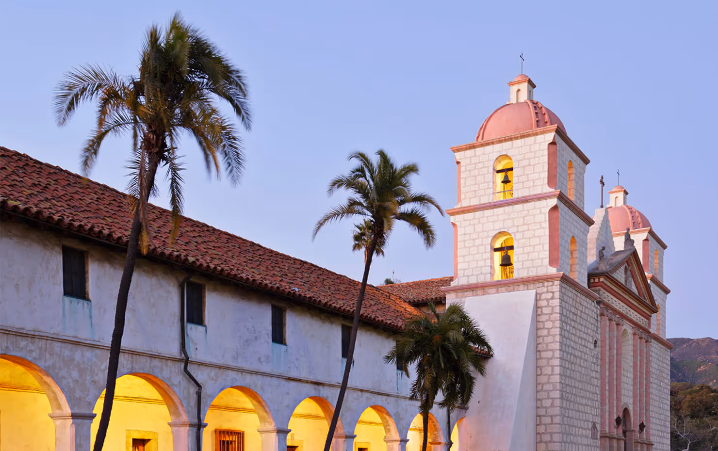 Waves crashing against rocky cliffs on a sandy beach at sunset with a calm sea horizon.