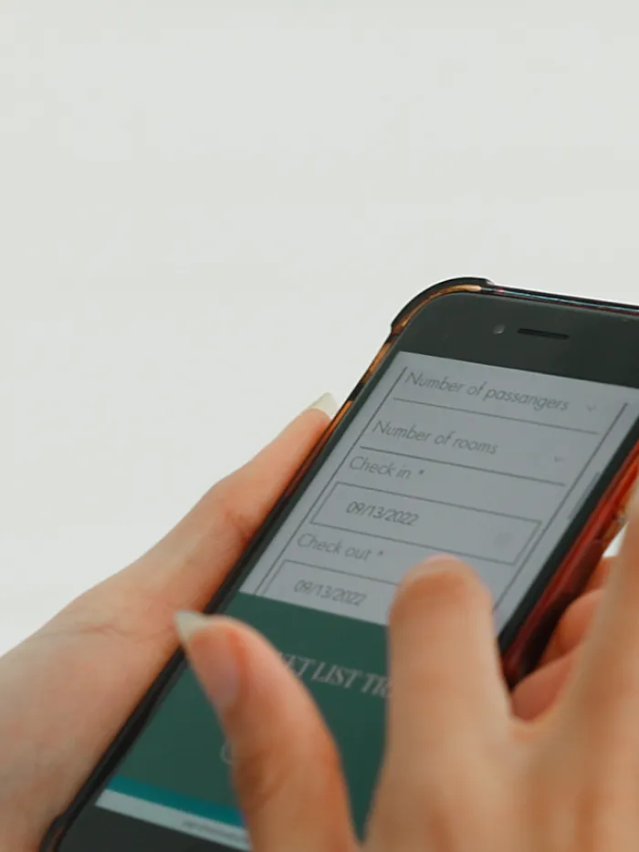 Hand using smartphone to fill out an online hotel booking form with check-in and check-out dates.