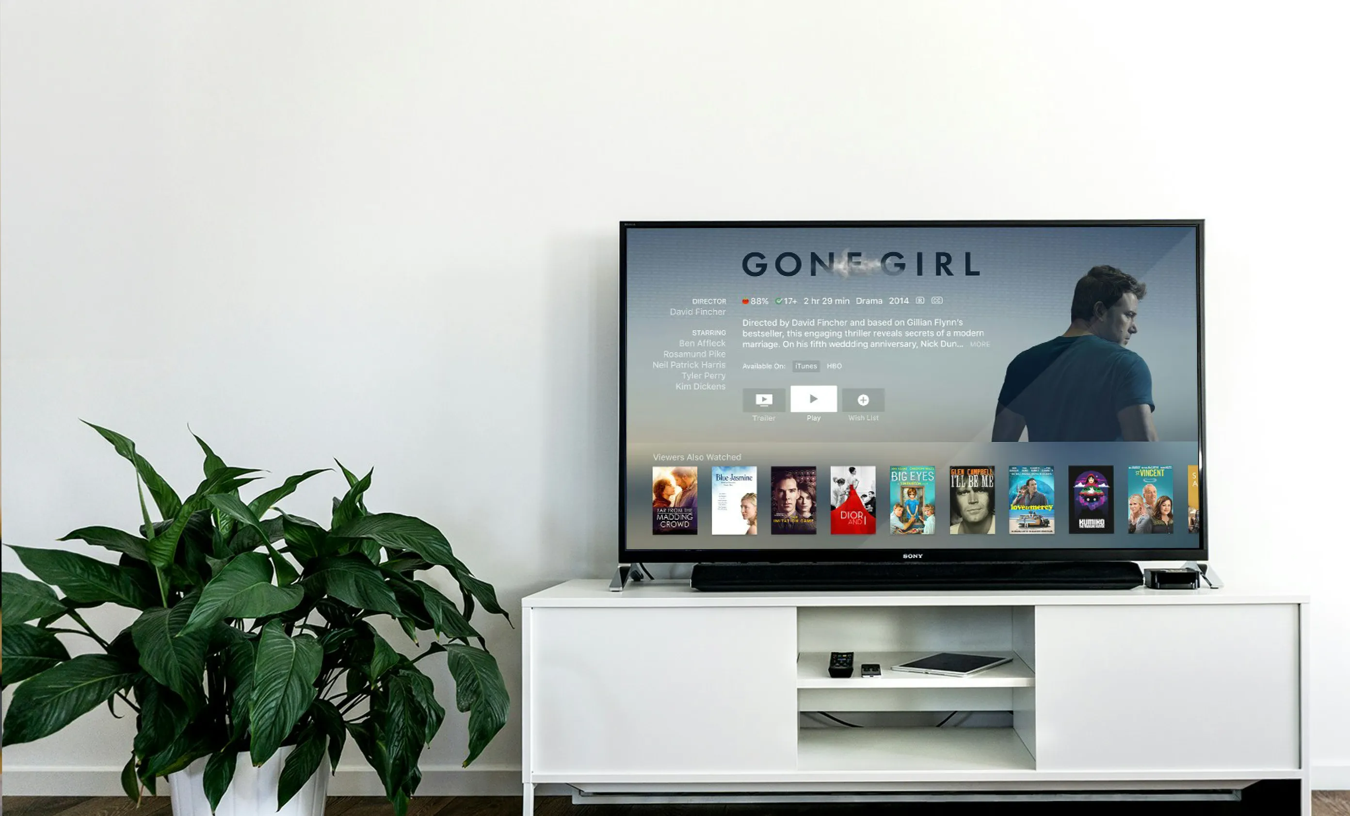 Modern living room with a large TV displaying the movie Gone Girl on a white media console beside a green potted plant.